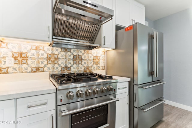 kitchen featuring tasteful backsplash, premium appliances, light hardwood / wood-style floors, white cabinetry, and range hood