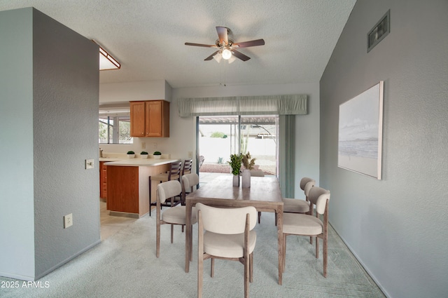 dining area featuring light carpet, a textured ceiling, and ceiling fan