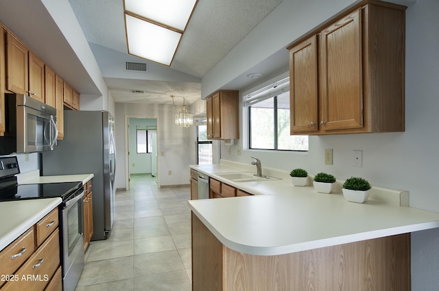 kitchen with pendant lighting, lofted ceiling, sink, kitchen peninsula, and stainless steel appliances