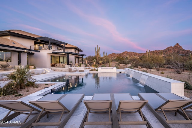 pool at dusk featuring pool water feature and a patio