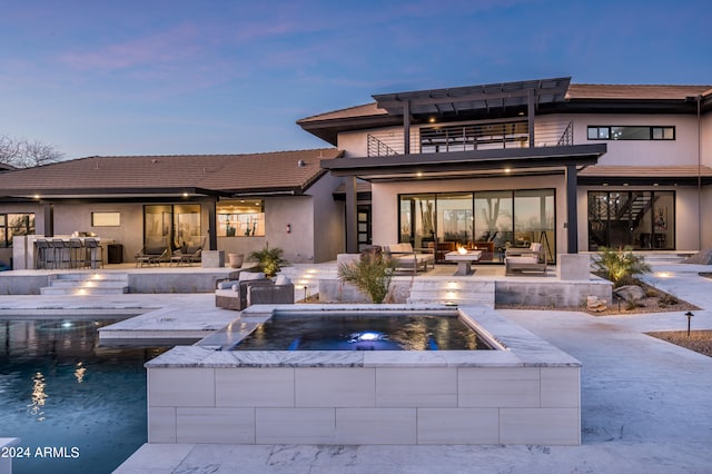 back house at dusk featuring a pool with hot tub, outdoor lounge area, and a patio area