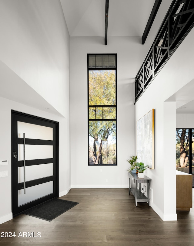 foyer entrance with dark hardwood / wood-style floors, beamed ceiling, and a high ceiling