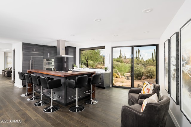 interior space with stainless steel double oven, a kitchen breakfast bar, dark hardwood / wood-style flooring, wooden counters, and wall chimney range hood