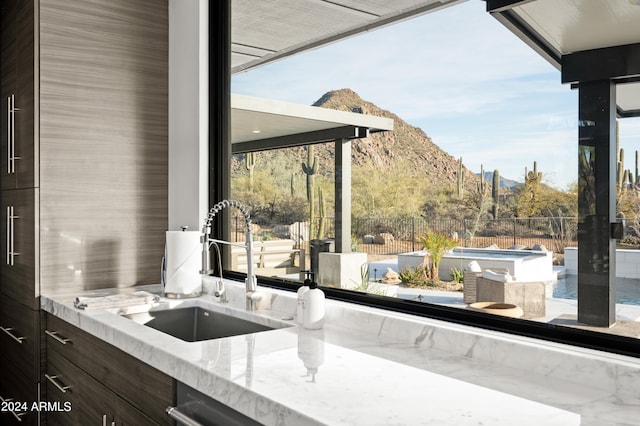 kitchen featuring light stone counters, dark brown cabinets, plenty of natural light, a mountain view, and sink