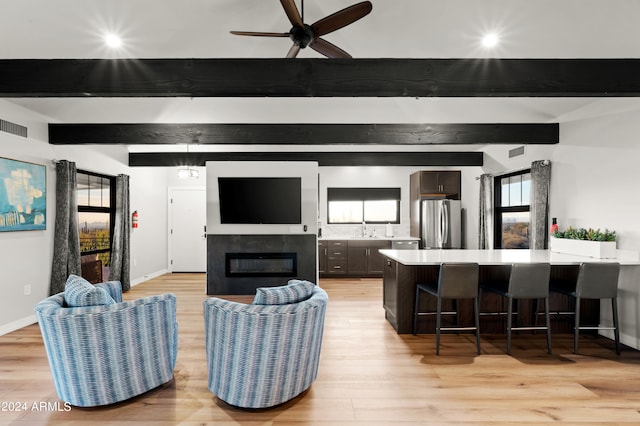 living room featuring beamed ceiling, light hardwood / wood-style floors, ceiling fan, and sink