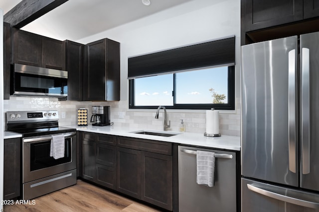 kitchen with appliances with stainless steel finishes, backsplash, light hardwood / wood-style floors, and sink