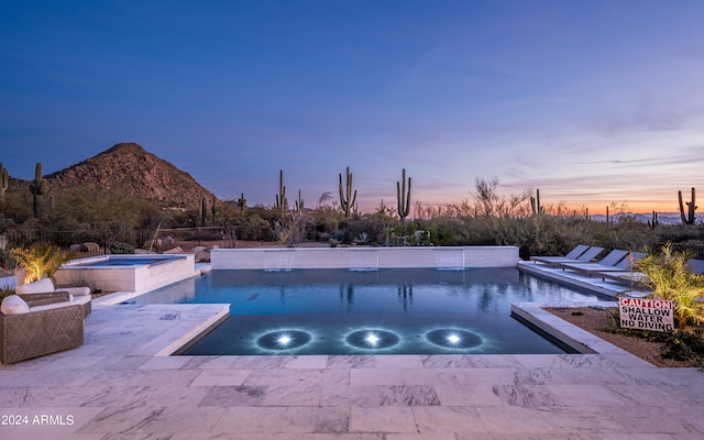 pool at dusk featuring a patio, a mountain view, and an in ground hot tub