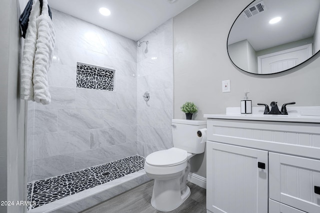 bathroom featuring vanity, a tile shower, hardwood / wood-style flooring, and toilet