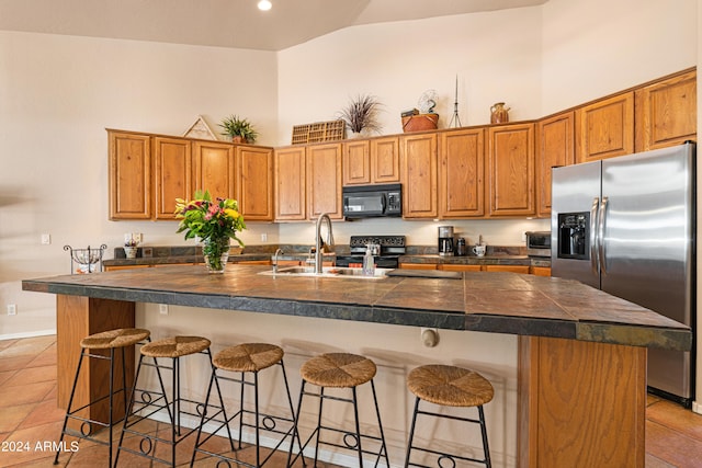 kitchen with a kitchen island with sink, black appliances, a breakfast bar area, and light tile patterned floors