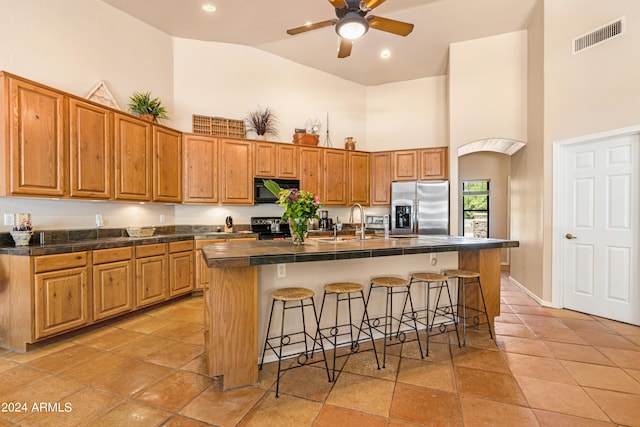 kitchen with electric stove, stainless steel refrigerator with ice dispenser, ceiling fan, a kitchen bar, and a center island with sink