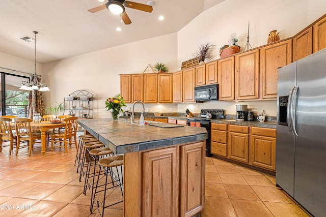 kitchen featuring a kitchen island with sink, ceiling fan with notable chandelier, black appliances, hanging light fixtures, and a breakfast bar