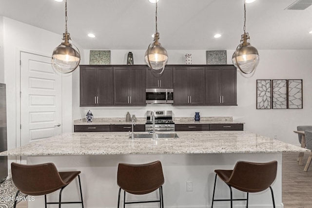 kitchen featuring a breakfast bar, a center island with sink, sink, appliances with stainless steel finishes, and dark brown cabinets