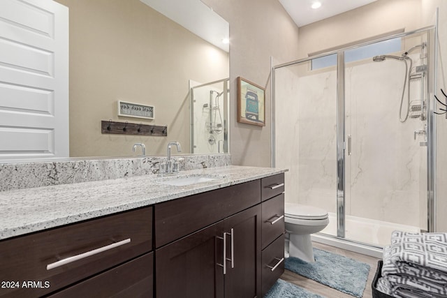 bathroom with hardwood / wood-style floors, vanity, toilet, and a shower with shower door