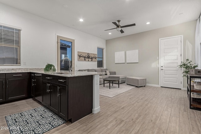 kitchen with kitchen peninsula, ceiling fan, sink, and light stone counters