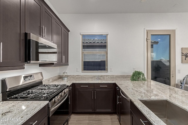 kitchen with light stone counters, dark brown cabinetry, sink, and appliances with stainless steel finishes