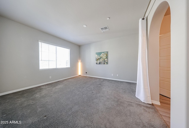 empty room with baseboards, carpet floors, visible vents, and arched walkways
