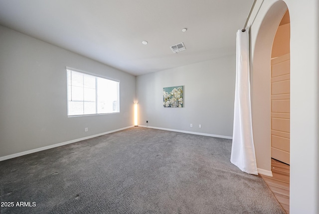 carpeted spare room featuring arched walkways, baseboards, and visible vents