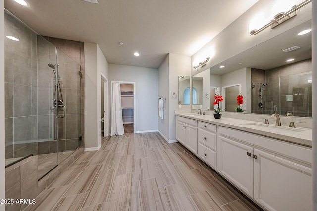 full bathroom featuring a walk in closet, double vanity, a stall shower, and a sink