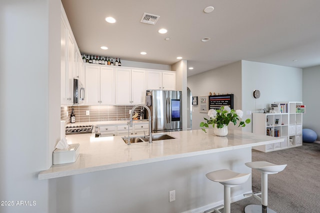 kitchen featuring sink, stainless steel appliances, white cabinets, a kitchen bar, and kitchen peninsula