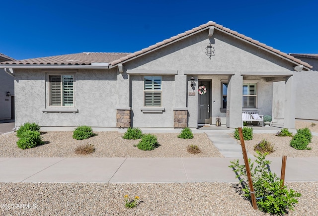 ranch-style home featuring a tile roof, covered porch, and stucco siding