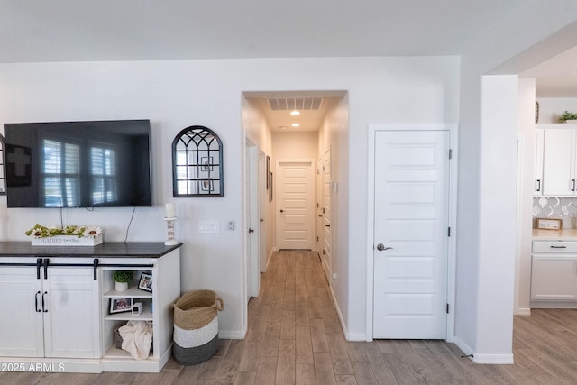 hallway featuring visible vents, baseboards, and light wood-style flooring