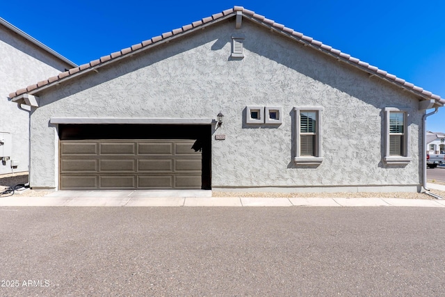 view of property exterior with a tiled roof, a garage, and stucco siding