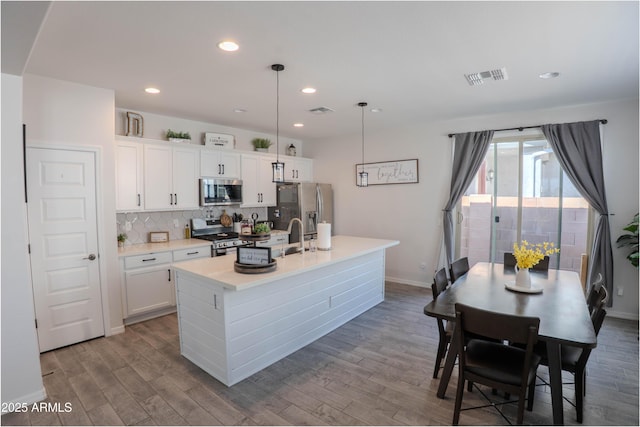 kitchen featuring visible vents, appliances with stainless steel finishes, wood finished floors, a center island with sink, and backsplash