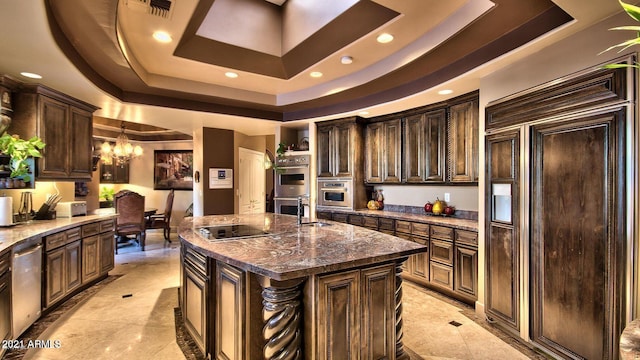 kitchen featuring a raised ceiling, dark brown cabinets, a kitchen island with sink, and stainless steel appliances