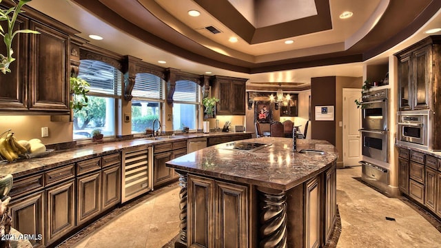 kitchen with beverage cooler, a raised ceiling, a center island with sink, sink, and appliances with stainless steel finishes