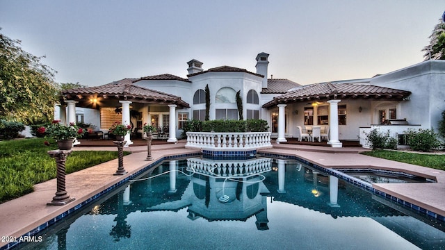 back house at dusk featuring a swimming pool with hot tub and a patio area