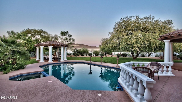 pool at dusk featuring a patio, a gazebo, a yard, and an in ground hot tub