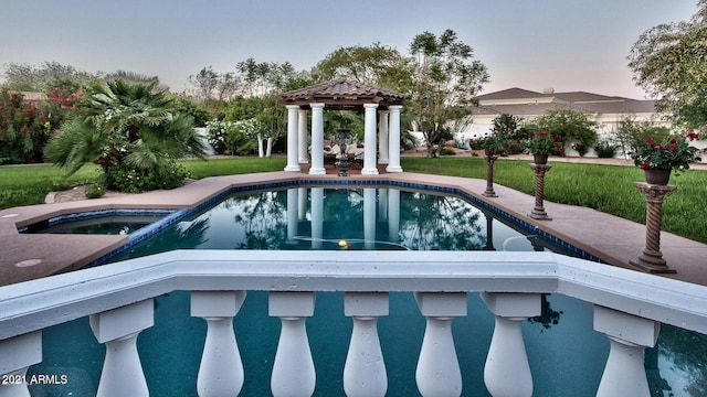 pool at dusk with a gazebo, a yard, and an in ground hot tub