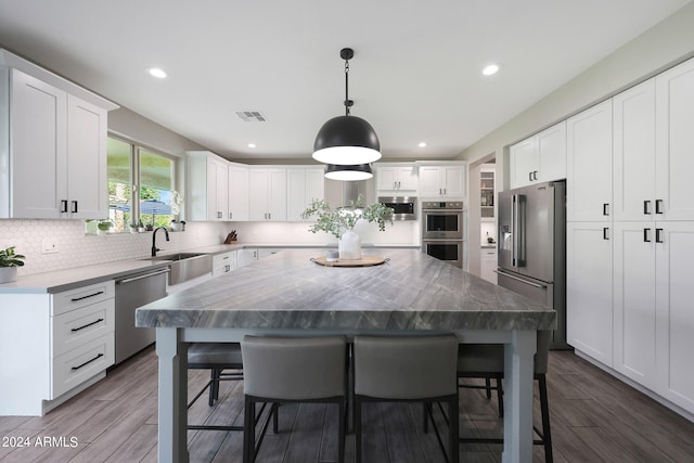 kitchen featuring appliances with stainless steel finishes, wood-type flooring, a kitchen island, and white cabinetry