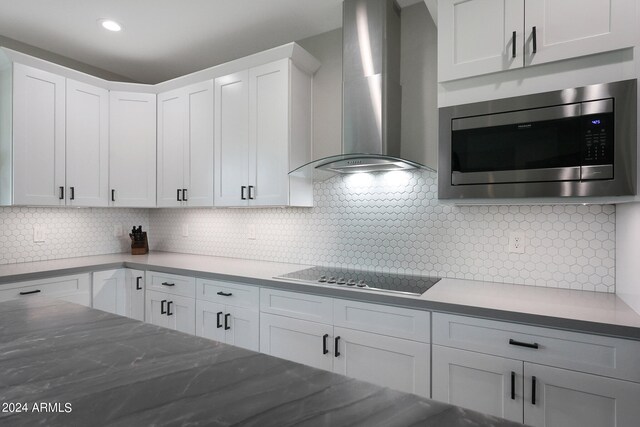 kitchen with tasteful backsplash, white cabinets, stovetop, stainless steel microwave, and wall chimney exhaust hood