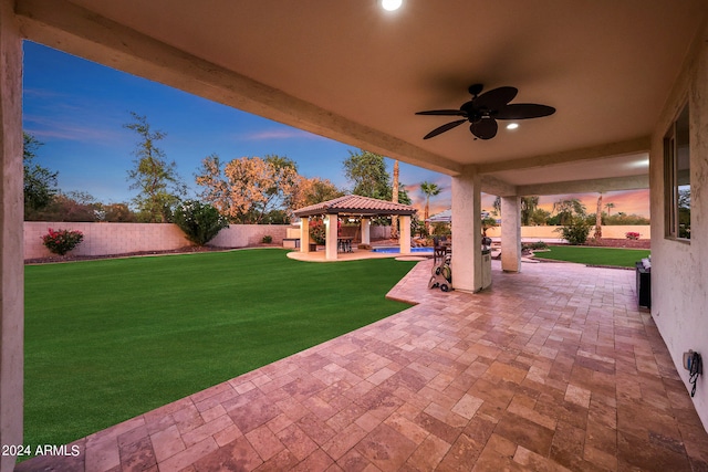 patio terrace at dusk featuring a lawn, a gazebo, and ceiling fan