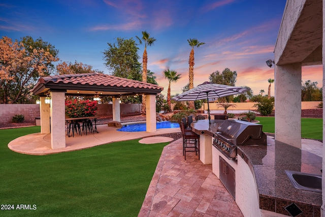 patio terrace at dusk with a lawn, a gazebo, an outdoor wet bar, and exterior kitchen