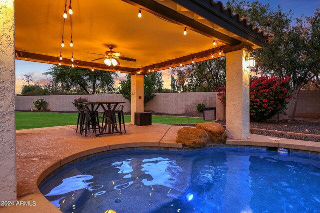 patio terrace at dusk featuring ceiling fan, area for grilling, an outdoor wet bar, and a grill