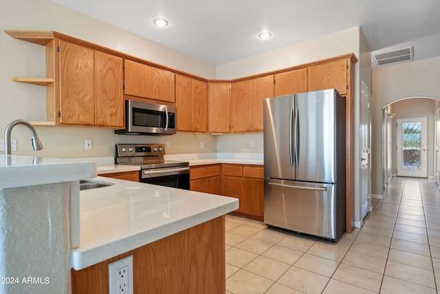 kitchen with appliances with stainless steel finishes, sink, kitchen peninsula, and light tile patterned flooring