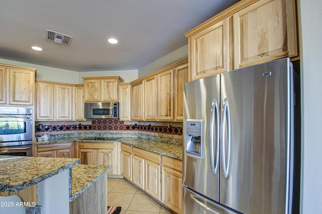 kitchen with dark stone countertops, stainless steel appliances, a kitchen breakfast bar, light tile patterned flooring, and decorative backsplash