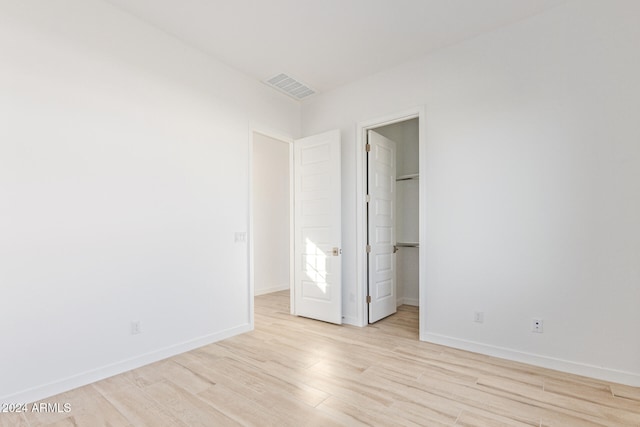 unfurnished bedroom with a closet, a spacious closet, and light hardwood / wood-style flooring