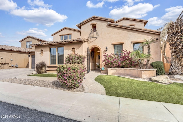 mediterranean / spanish house featuring a garage, a tiled roof, a front yard, and stucco siding