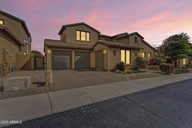 mediterranean / spanish-style house with a tiled roof, decorative driveway, an attached garage, and stucco siding