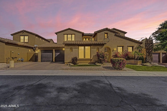 mediterranean / spanish-style home with a garage, driveway, a tiled roof, and stucco siding