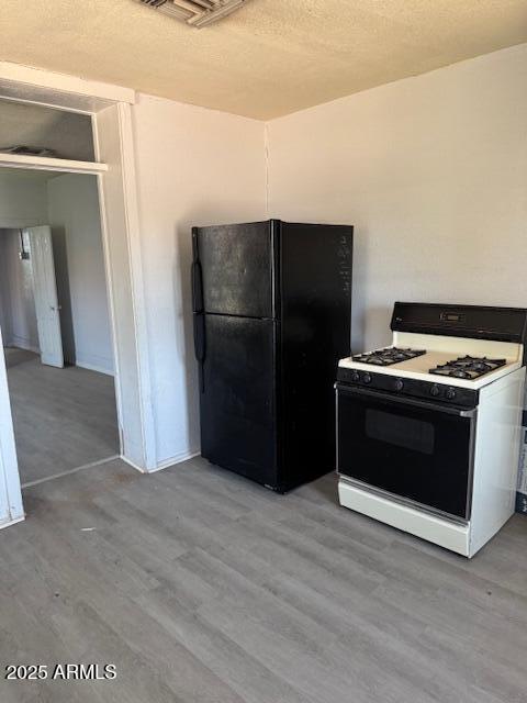 1220 N F Ave, Douglas, AZ 85607 - kitchen with white range with gas stovetop, freestanding refrigerator, light wood-type flooring, and a textured ceiling