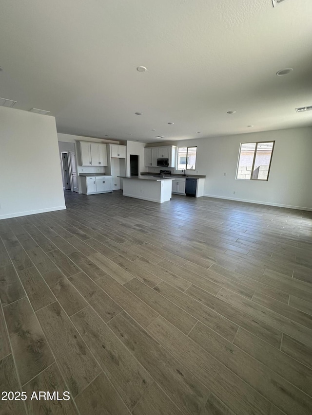 unfurnished living room with visible vents, dark wood-style floors, and baseboards