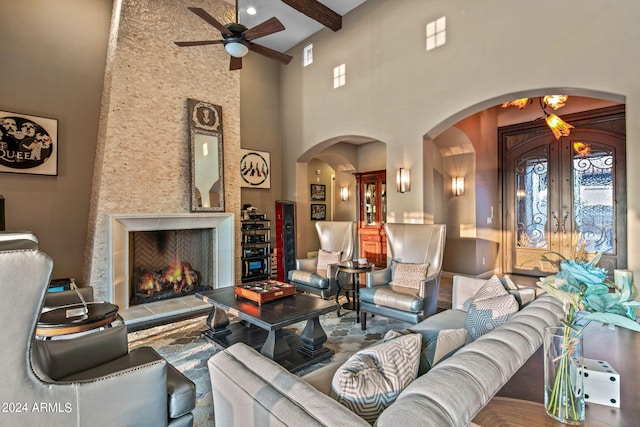 living area featuring ceiling fan, beam ceiling, arched walkways, a towering ceiling, and a lit fireplace