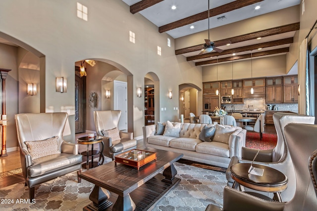 living room with ceiling fan, visible vents, arched walkways, beamed ceiling, and a high ceiling