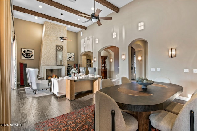 dining area featuring ceiling fan, arched walkways, a fireplace, beamed ceiling, and a high ceiling
