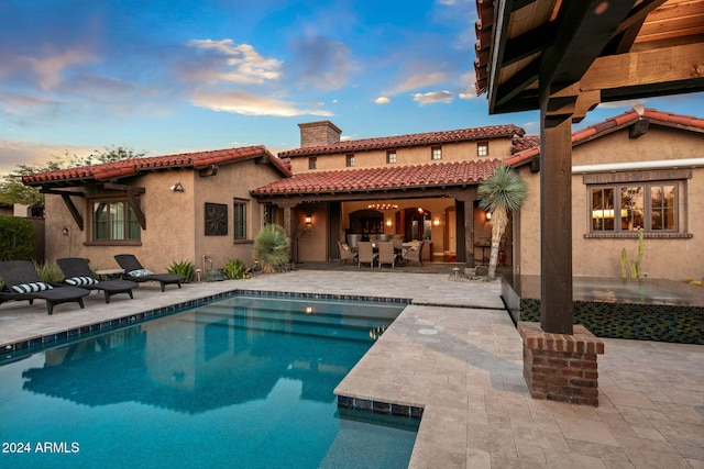 back of property featuring stucco siding, an outdoor pool, a chimney, a patio area, and a tiled roof