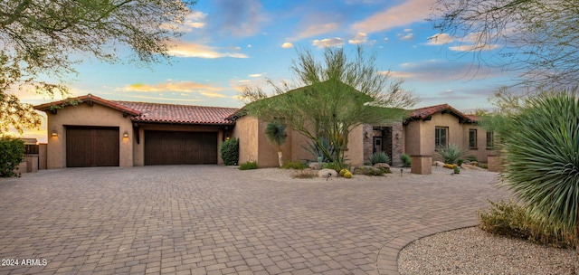 mediterranean / spanish-style home featuring stucco siding, decorative driveway, a tiled roof, and a garage